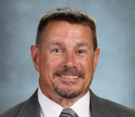 man wearing a grey suit jacket and tie smiling into the camera for his headshot photo