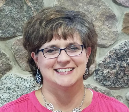 woman wearing a pink shirt and glasses smiling into the camera